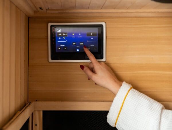 A woman using a Sirona 3-Person Hemlock Infrared Sauna with 8 Carbon Heaters to control an infrared sauna.