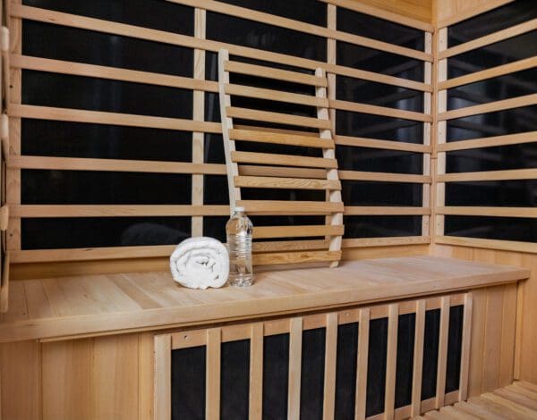 A Sirona 3-Person Hemlock Infrared Sauna with 8 Carbon Heaters, wooden slats and a bottle.